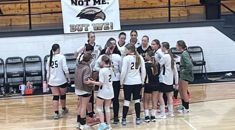 Falkner volleyball players gather in a team huddle beside the bench.