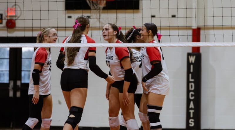 Volleyball players in red and white Wildcats uniforms gather beside the net.